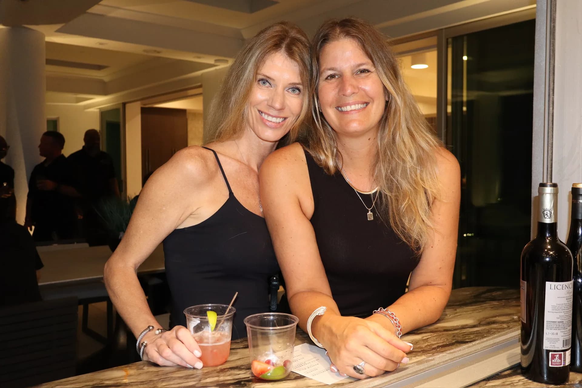 Two bartenders smiling behind marble bar with cocktails at birthday party