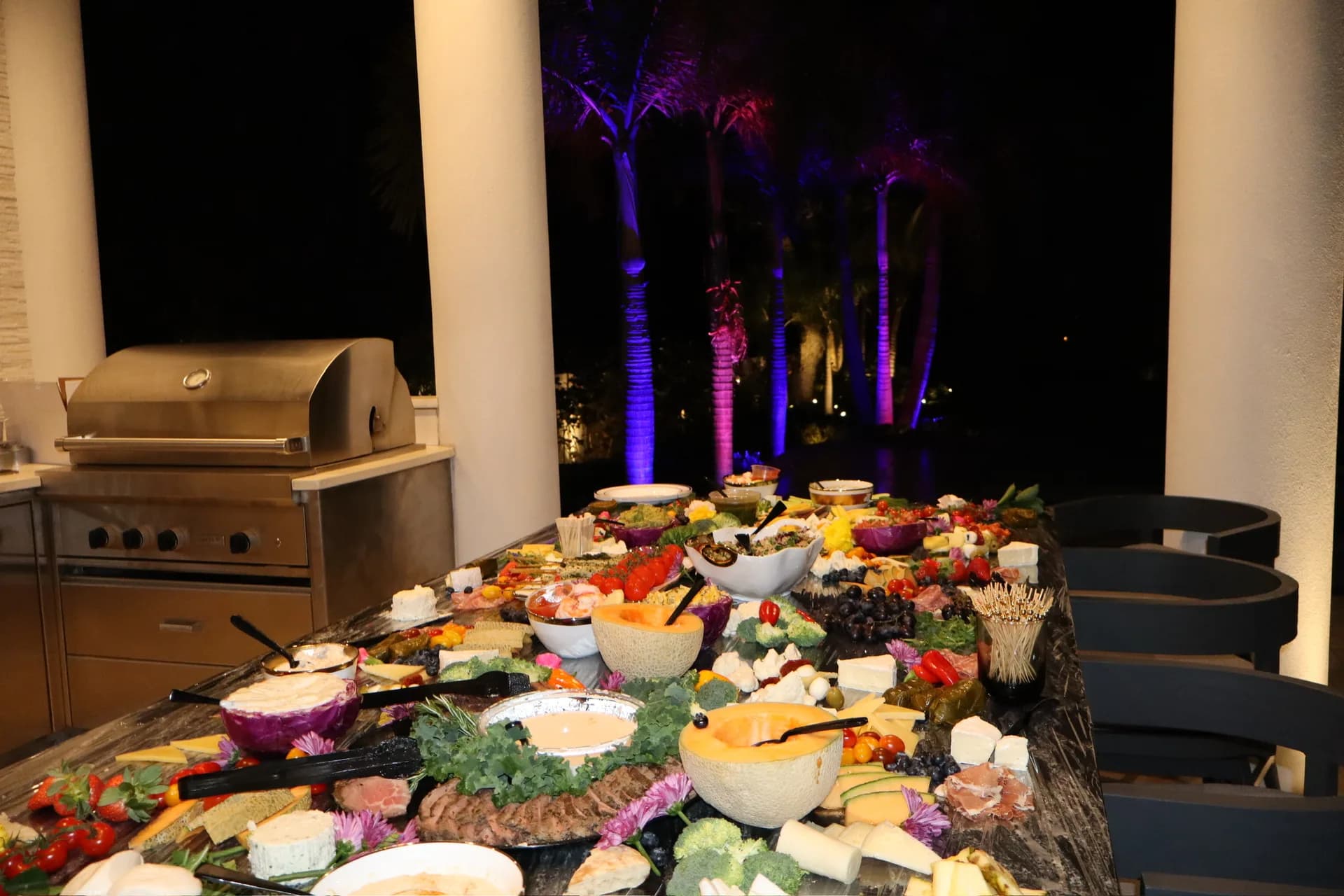 Elaborate charcuterie spread at outdoor birthday party with purple uplighting