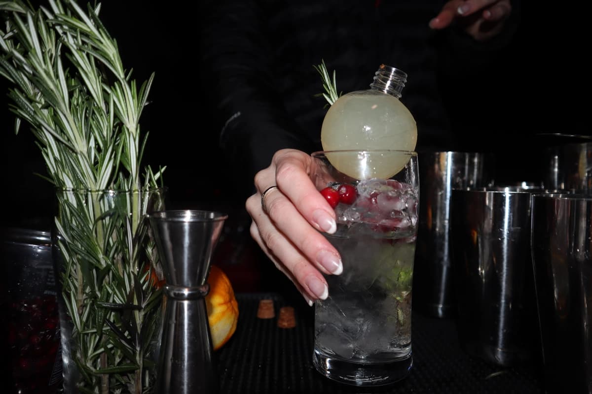 Bartender crafting cranberry cocktail with ice sphere garnish at Christmas party
