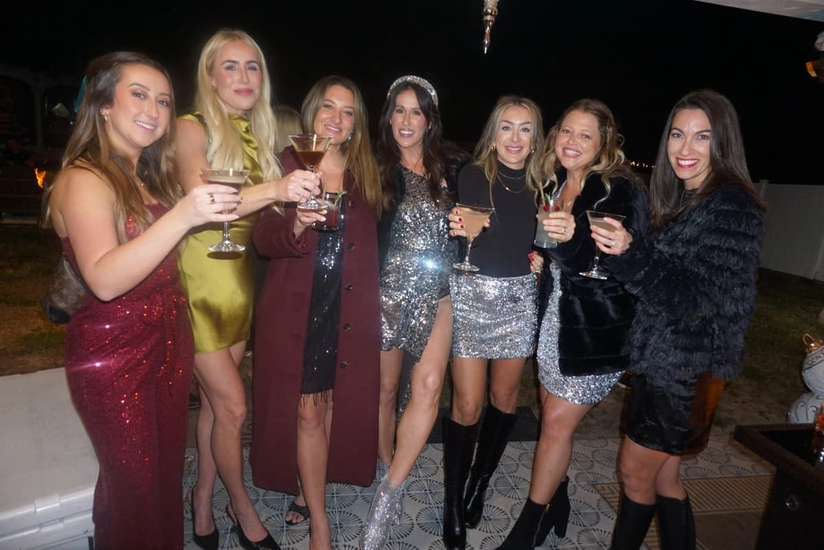 Group of friends toasting cocktails in sparkly dresses at Christmas party