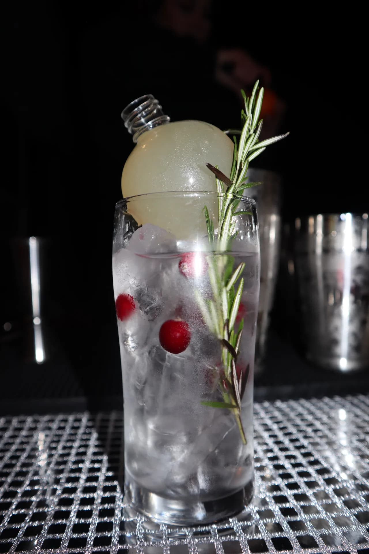 Tall cocktail with ice sphere, cranberries, and rosemary sprig