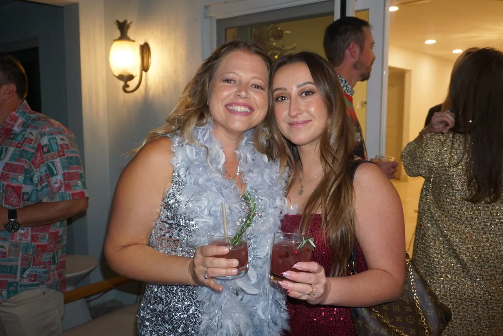Two friends posing with cranberry cocktails wearing holiday feather boa