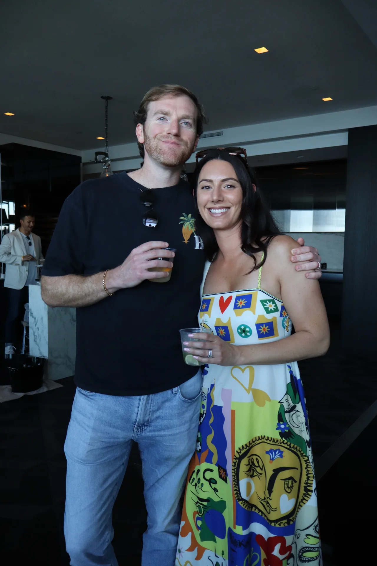 Couple posing with drinks in colorful outfit at penthouse party