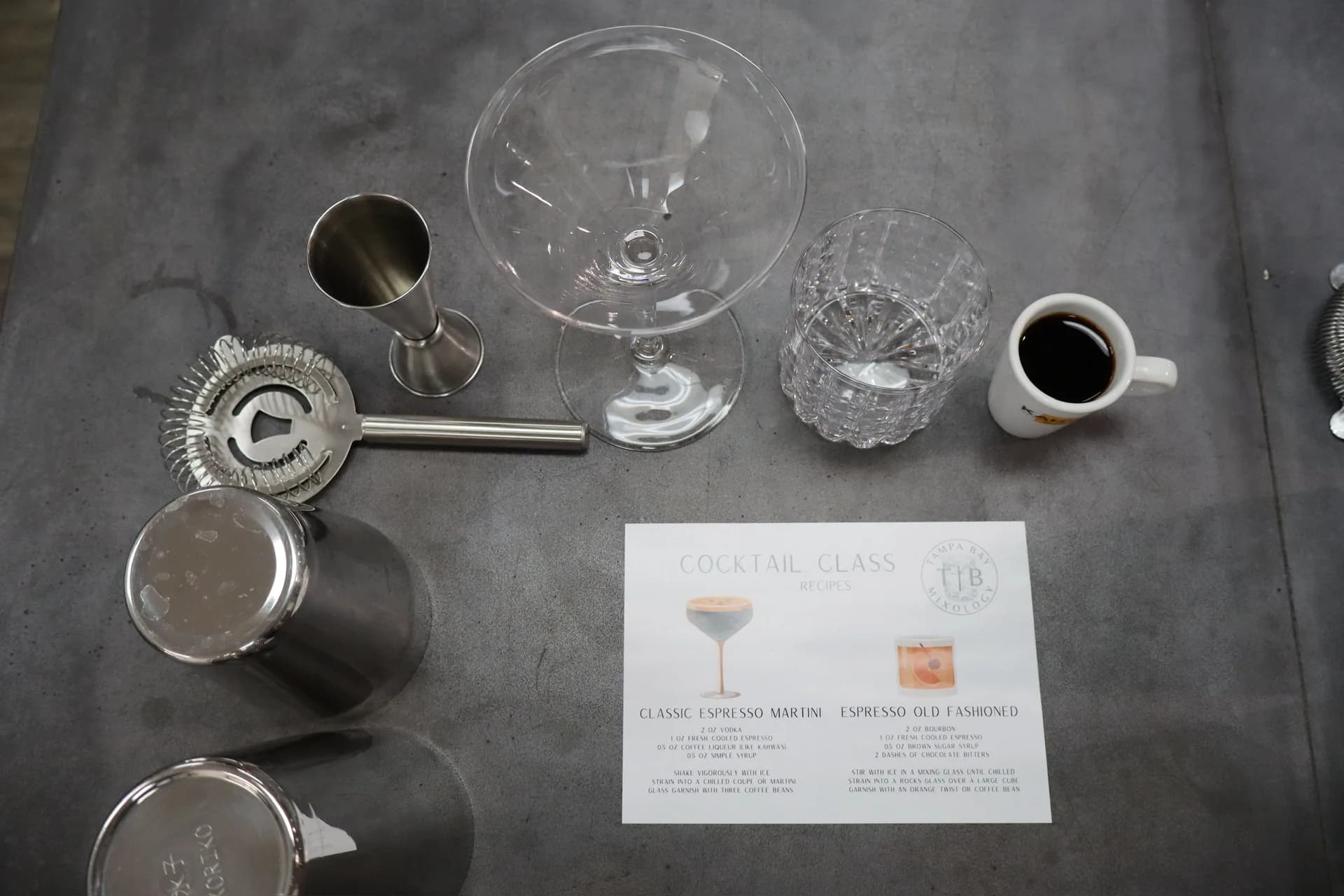 Cocktail class place setting with bar tools, glassware, and espresso menu card