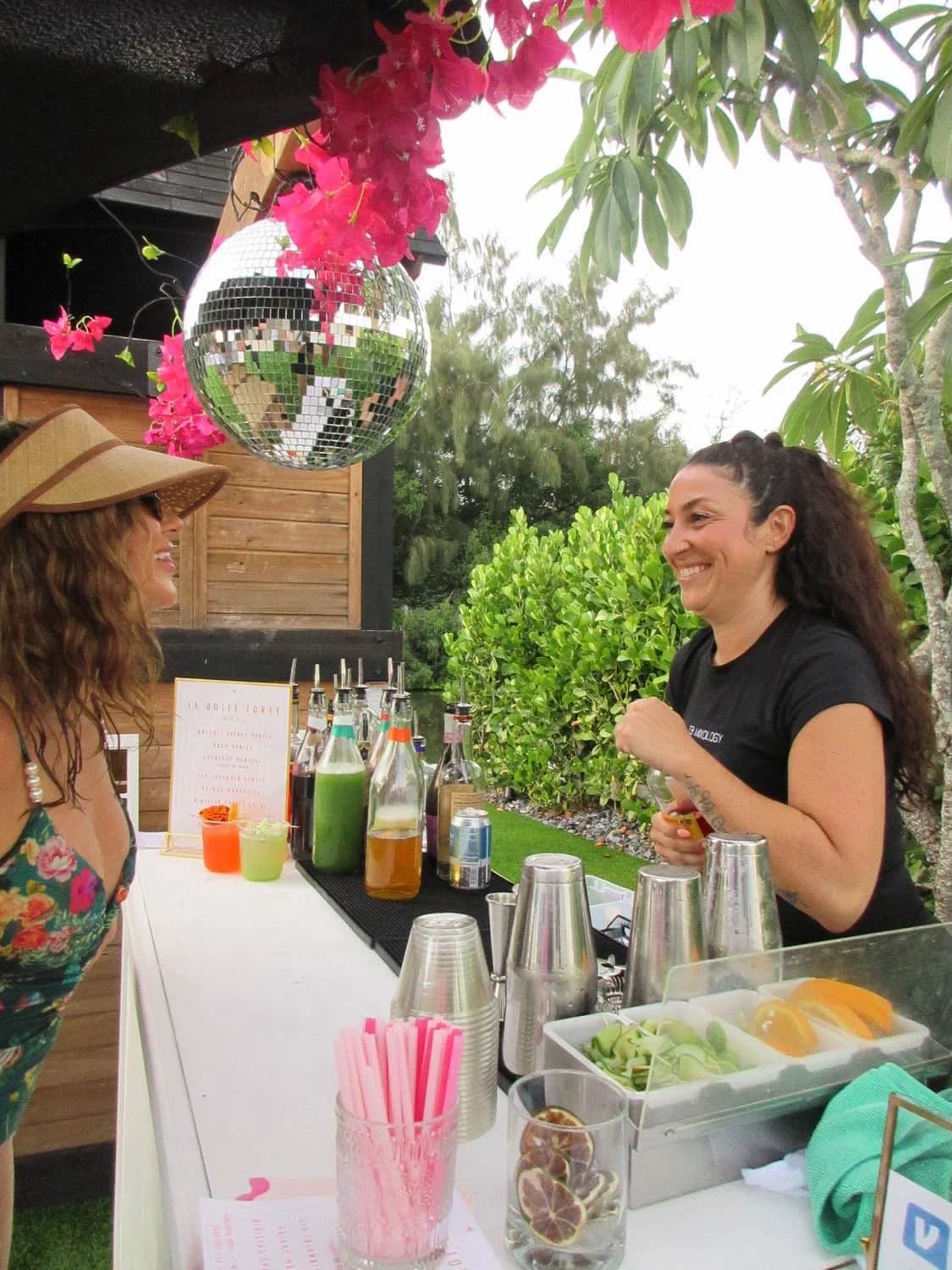 TB Mixology bartender at a white outdoor bar under a disco ball and bougainvillea