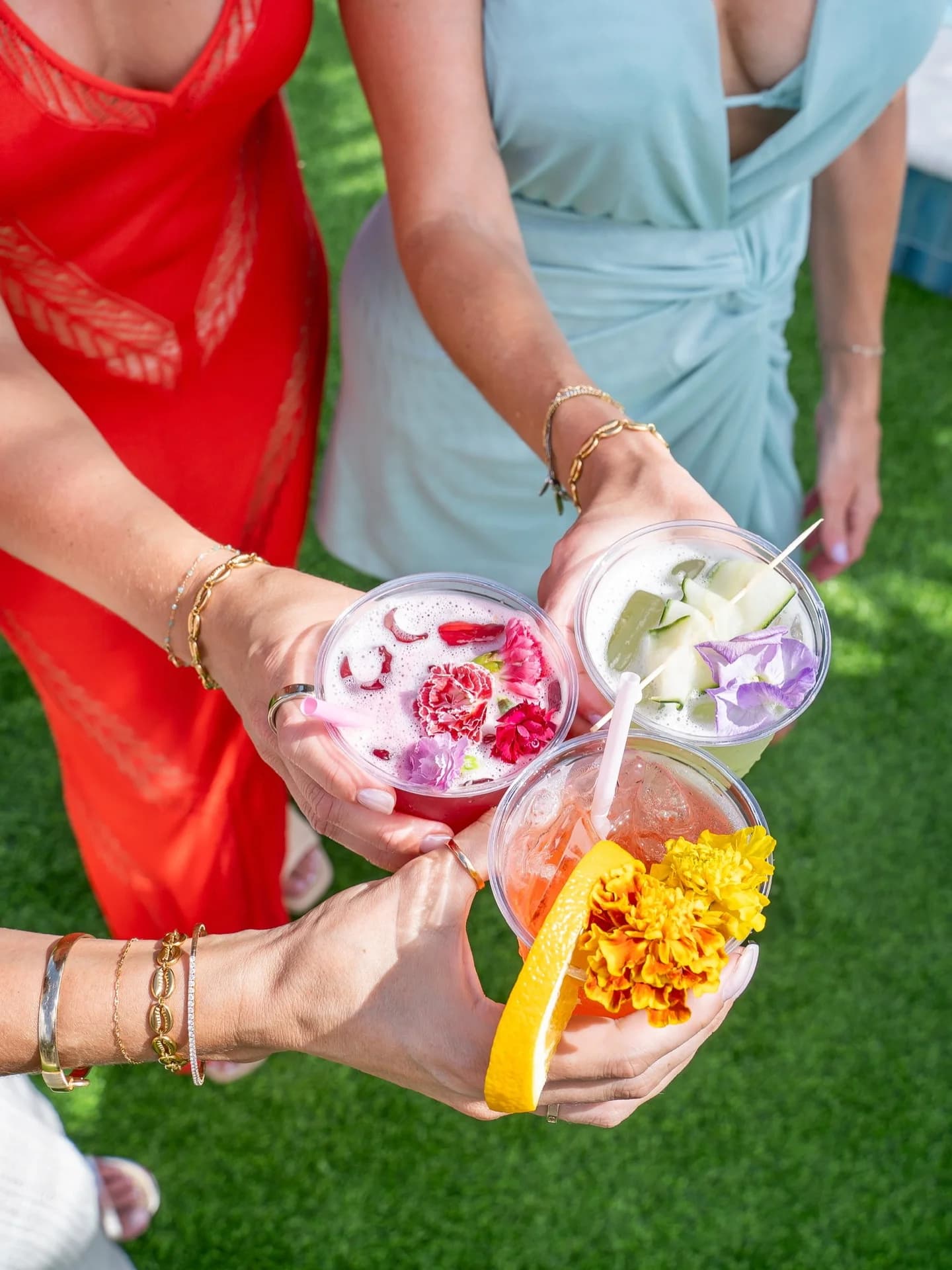 Three cocktails topped with edible flowers held together over a green lawn