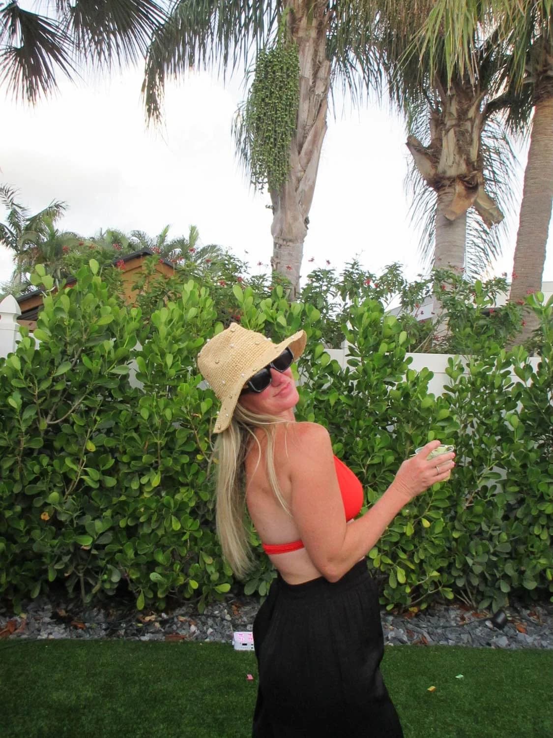 Guest in a straw hat holding a cocktail among palm trees