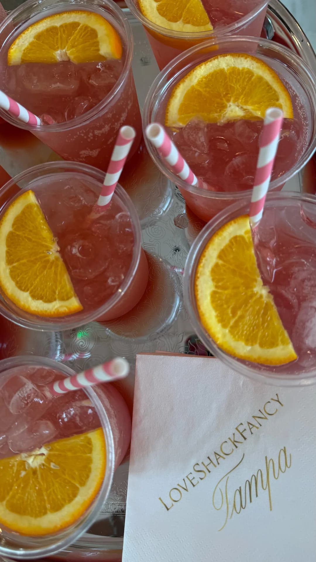 Overhead tray of pink cocktails with orange slices and a LoveShackFancy Tampa napkin