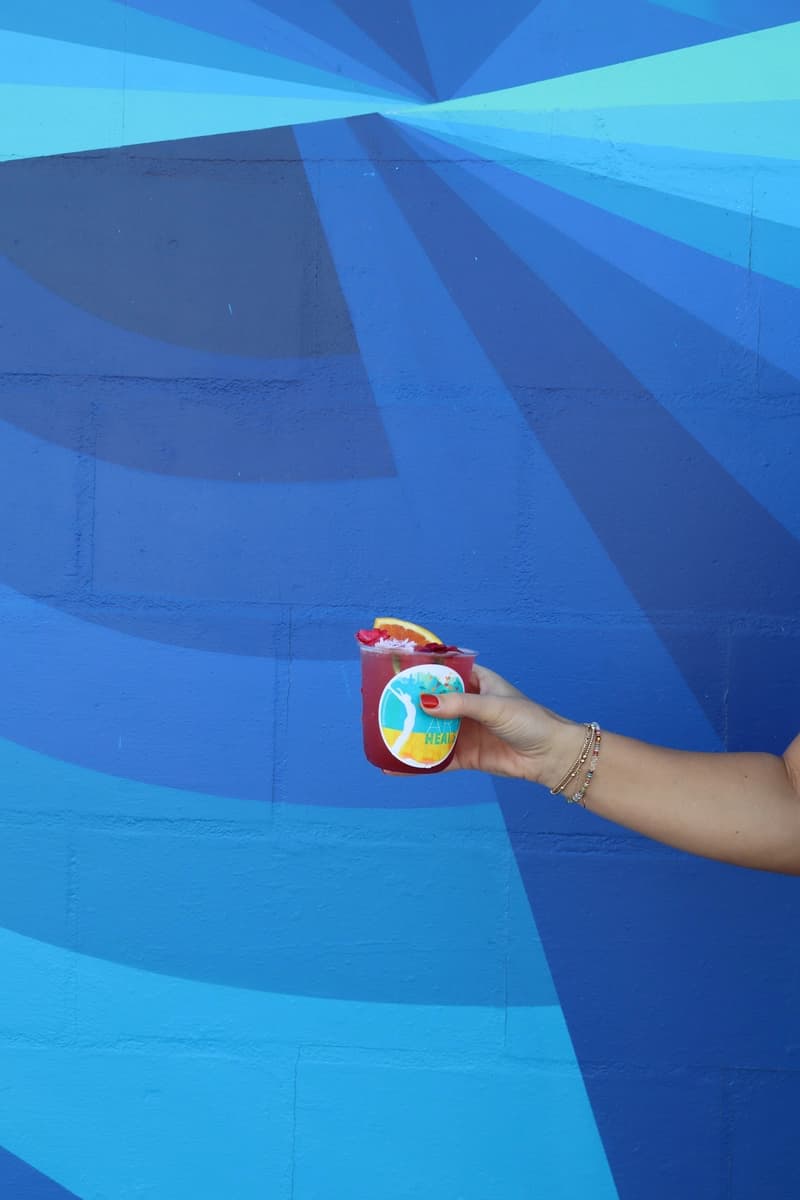 Pink mocktail held against blue geometric mural at Art Heals event