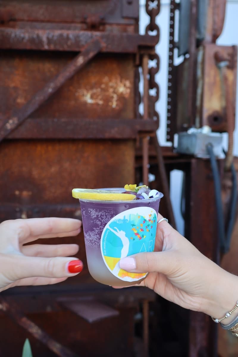 Purple mocktail with Art Heals branding against industrial metal backdrop