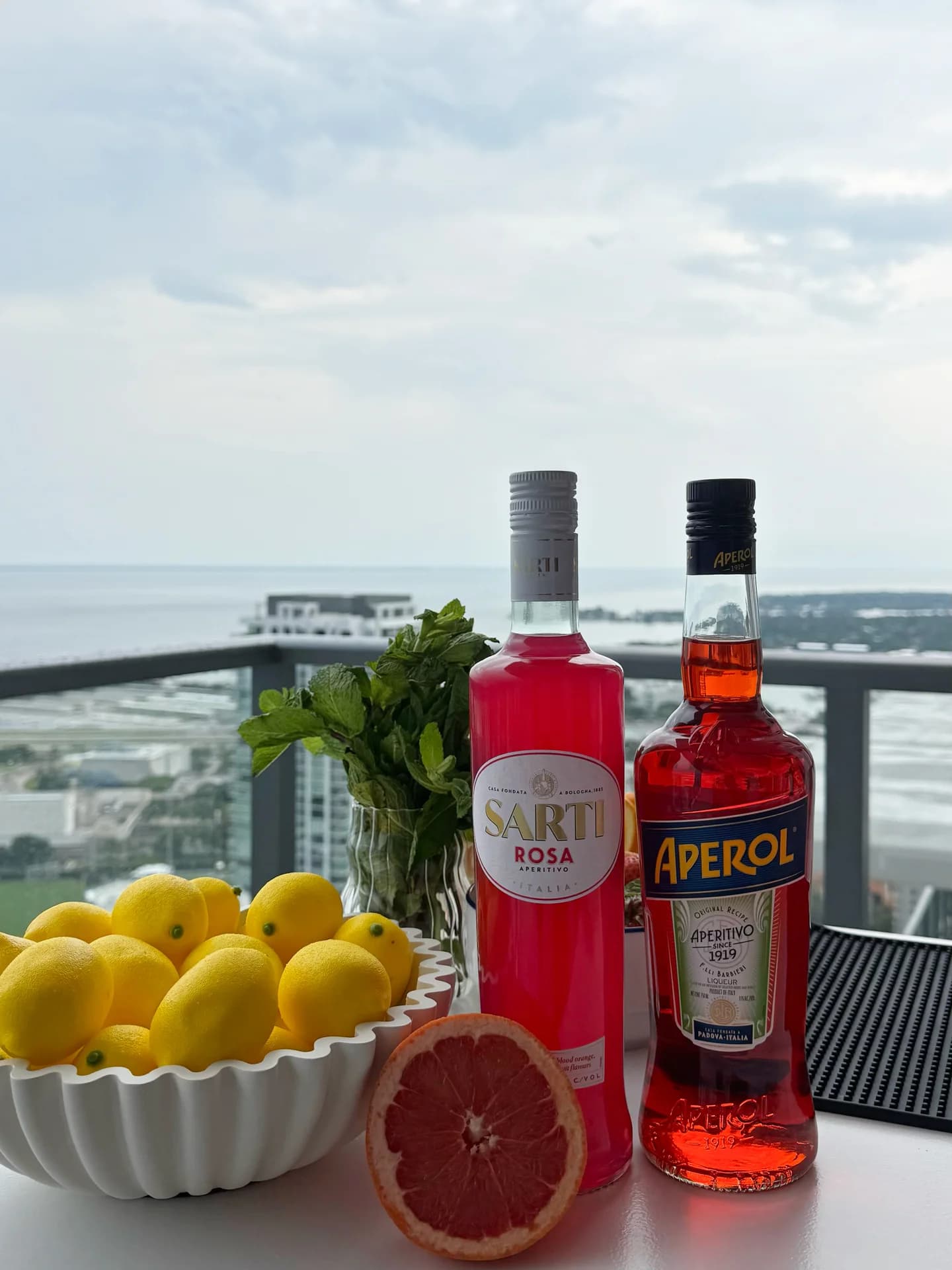 Sarti Rosa and Aperol bottles with lemons, mint, and grapefruit on the bar