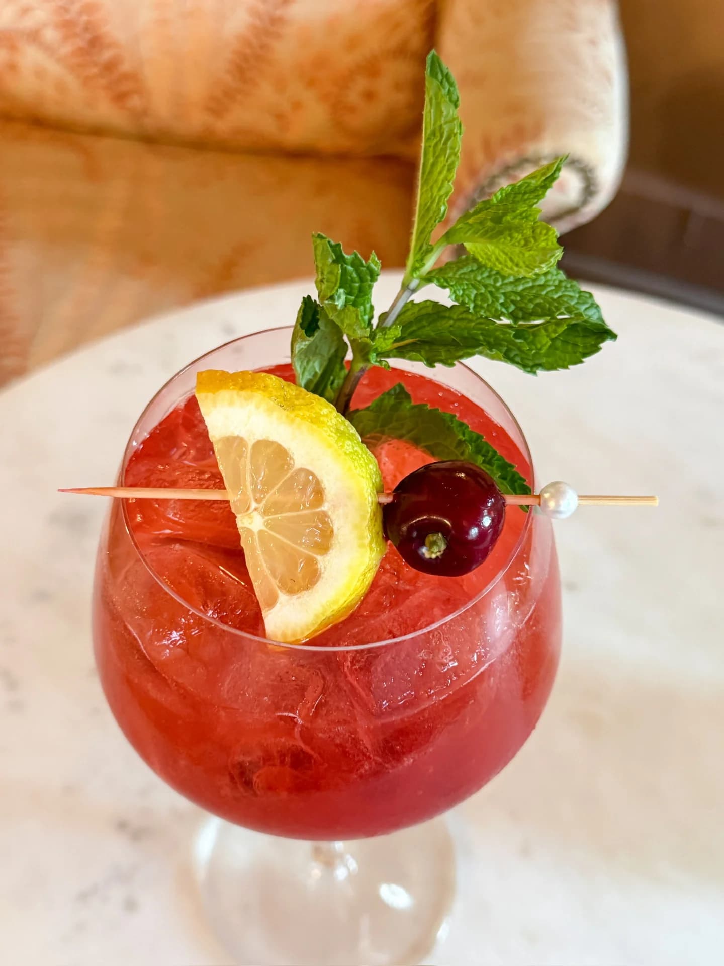 Red berry cocktail garnished with mint, lemon wheel, and cherry