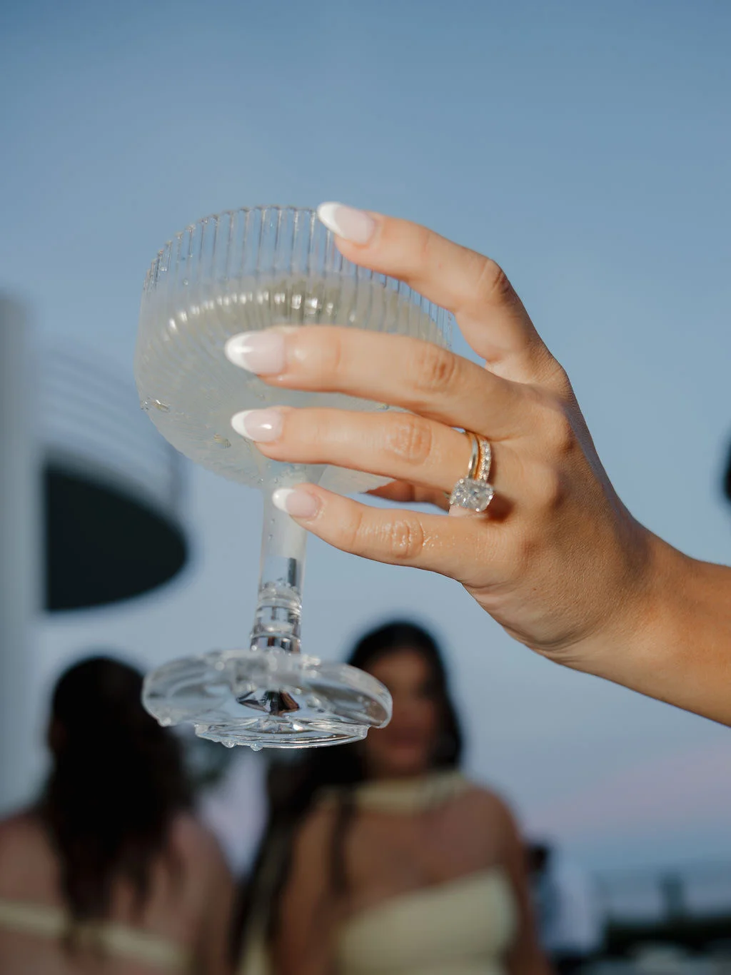 Bride's hand with wedding ring holding a fluted champagne coupe