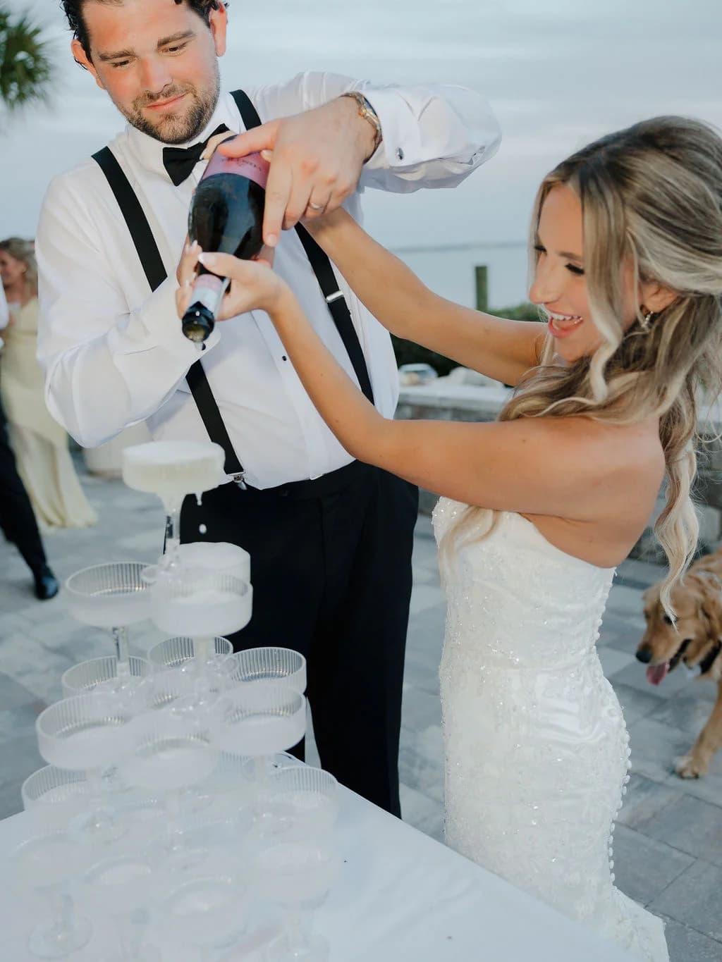 Bride and groom pouring champagne into a coupe tower at their wedding reception