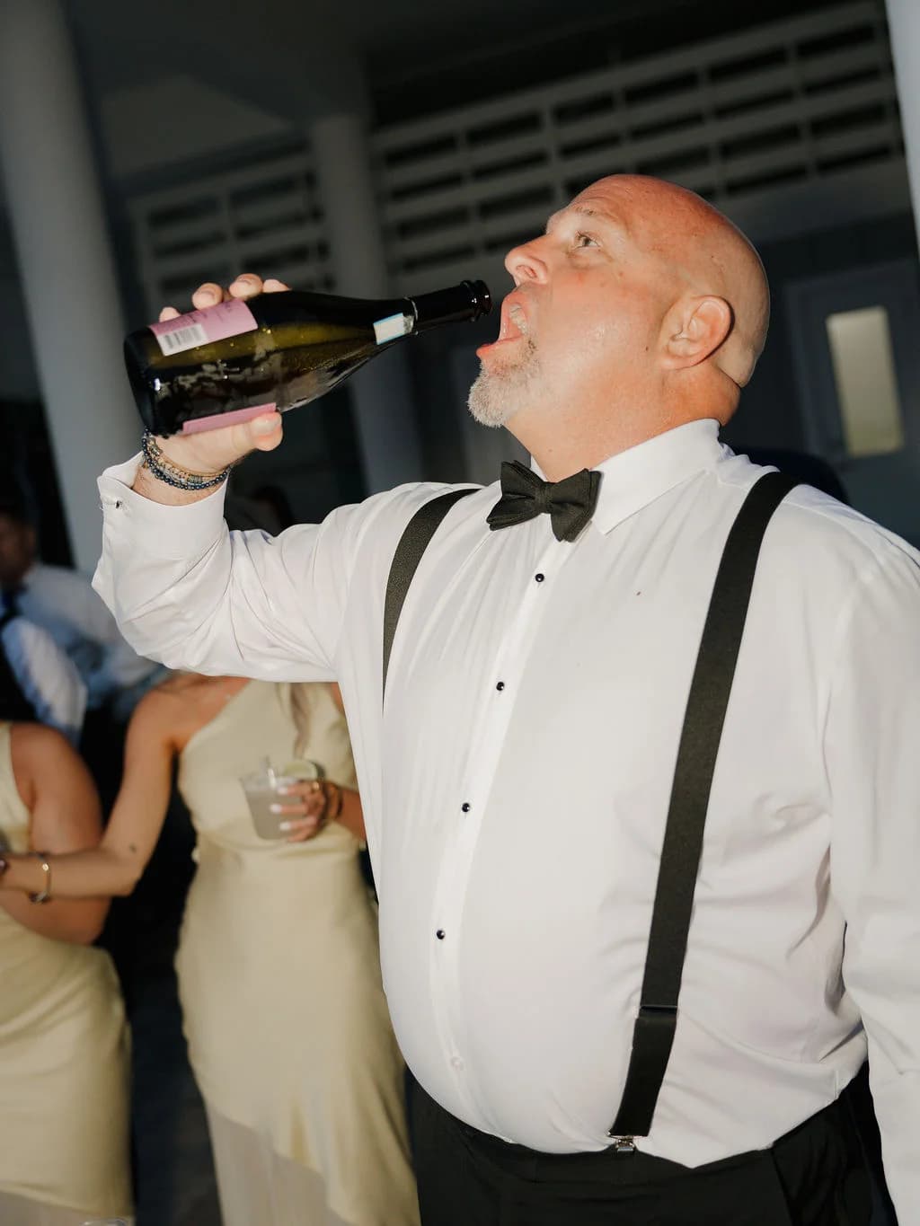 Wedding guest in bow tie and suspenders drinking champagne at the reception