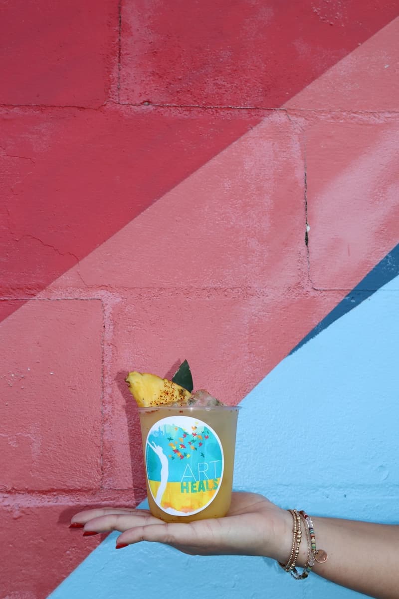 Pineapple mocktail held against colorful mural at Art Heals event